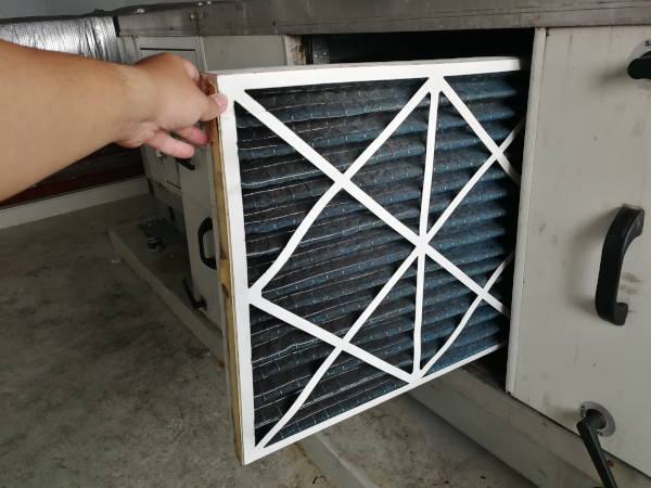 Homeowner pulling a dirty pleated furnace filter out of an HVAC air handler
